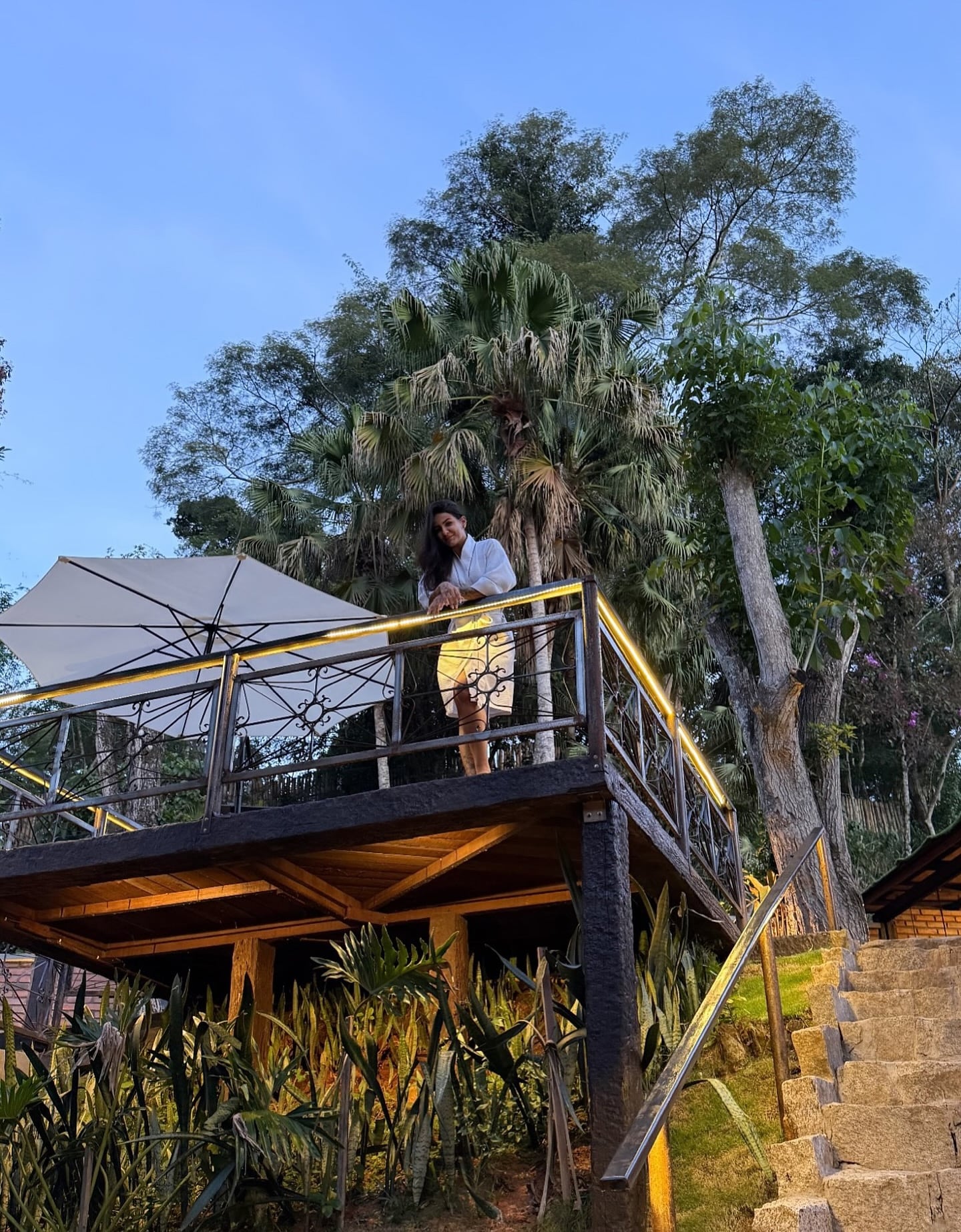 Deck suspenso entre cafe e árvores nativas, com ombrelone branco aberto