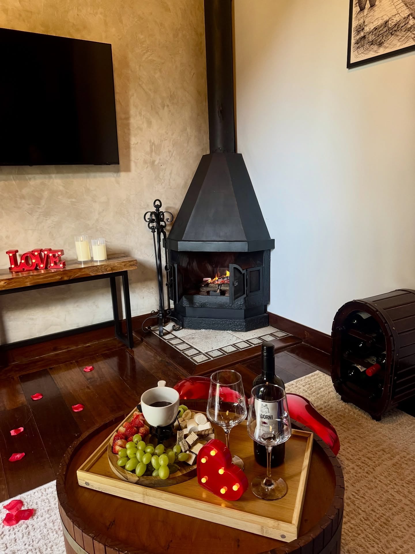 Lareira de ferro acesa na sala, com bandeja de vinho, queijos e uvas na mesa de centro