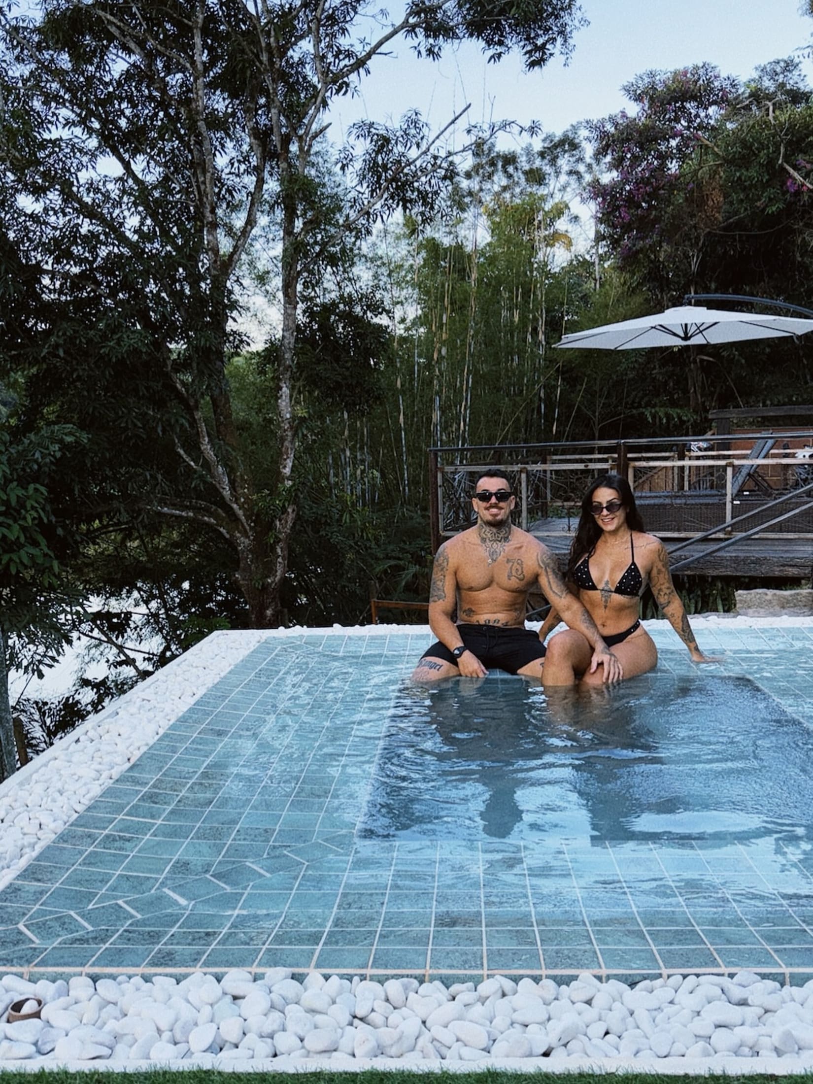 Piscina de borda azulejada no deck elevado, com ombrelone e a marrom fechada ao fundo