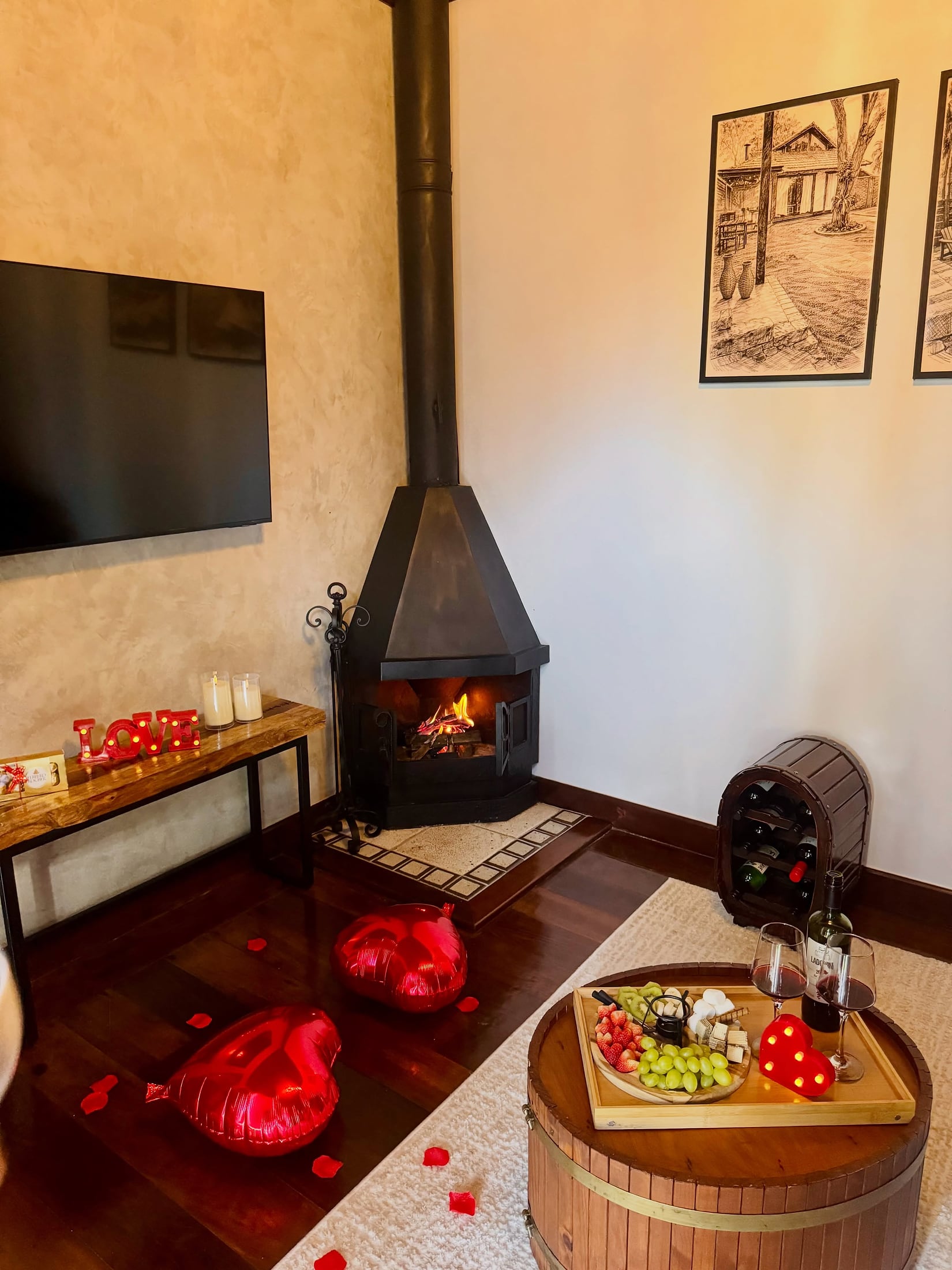 Sala do bangalô com lareira acesa, televisão na parede e adega de madeira ao lado