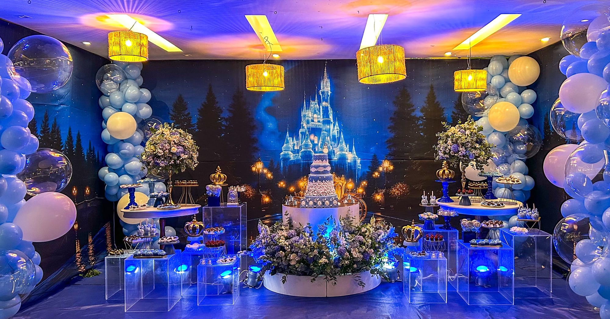 Cenário noturno de castelo iluminado com balões azuis e lustres, pronto para a festa