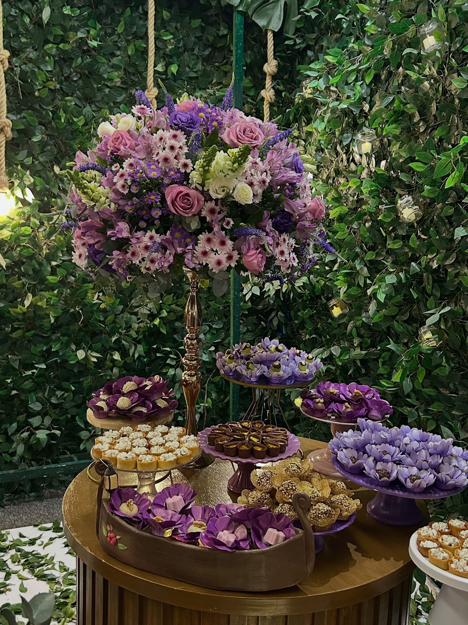 Bandeja de doces finos em forminhas lilás com um arranjo alto de flores