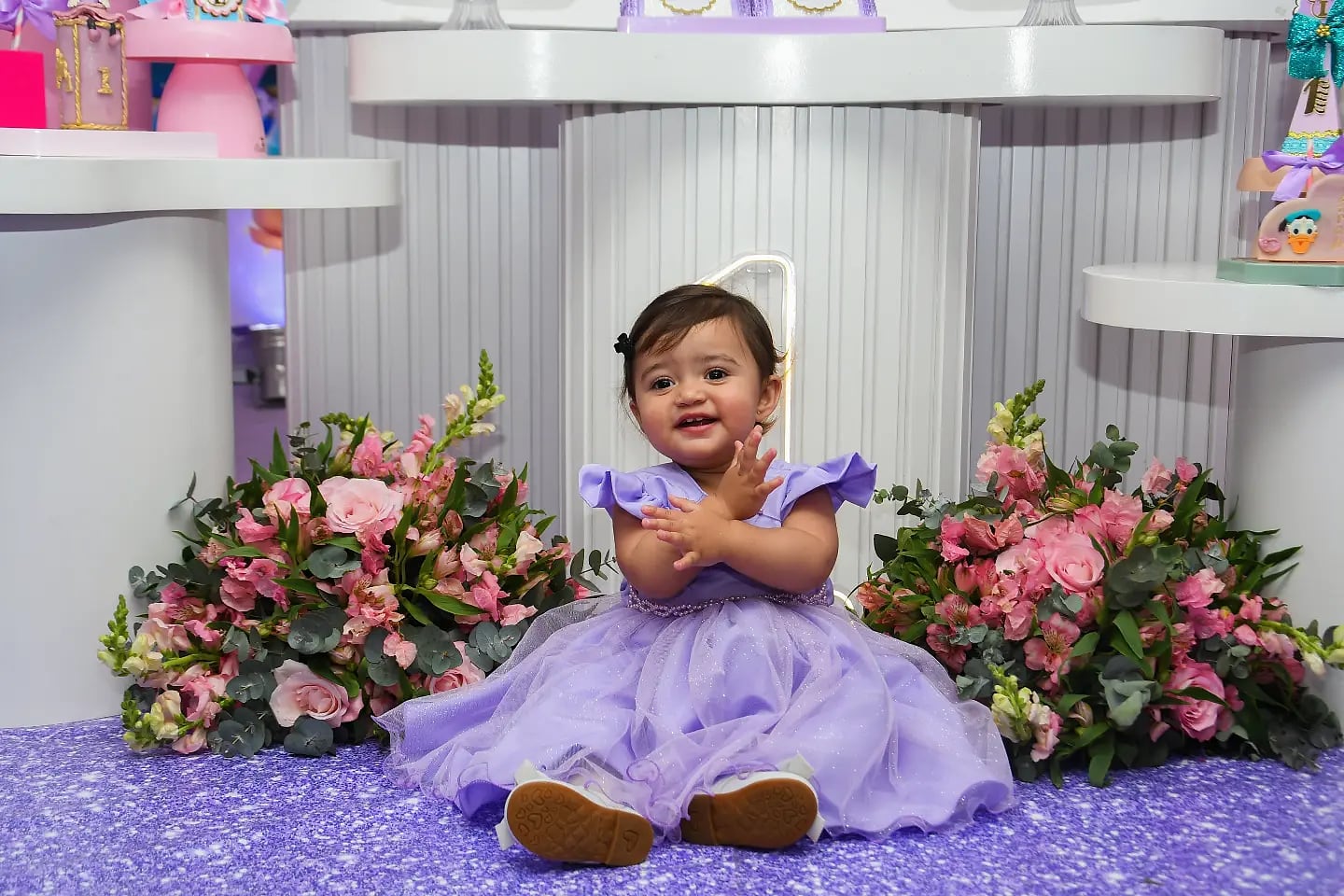 Aniversariante de vestido lilás sentada entre arranjos de flores rosa