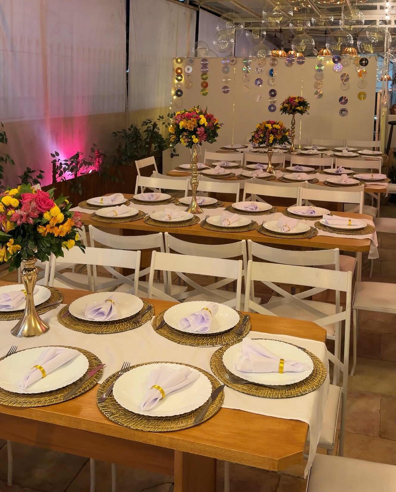 Salão da Via Festas com mesas postas, sousplats dourados e arranjos de flores